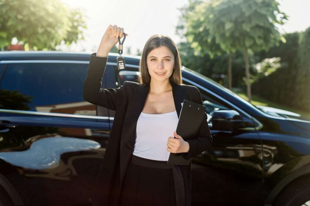 Beautiful girl with car key in hand. Caucasian woman car seller holding car keys, standing in front